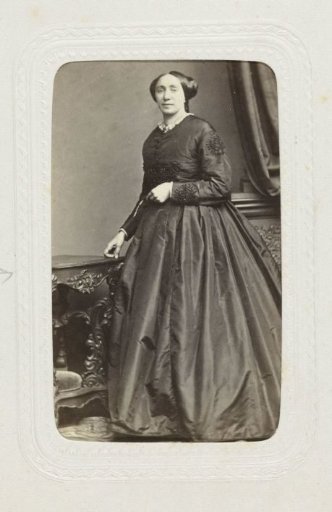 Studio portrait of a standing lady in a long dress next to a table