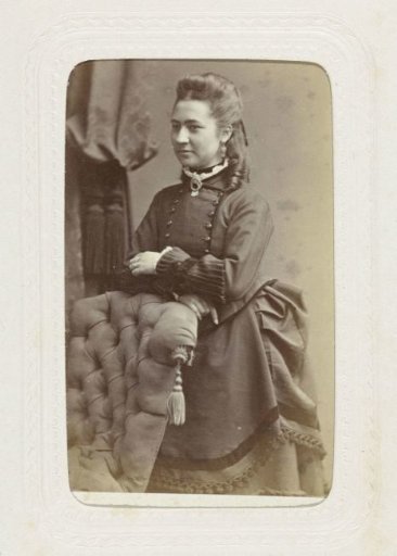 Studio portrait of a standing young woman in a black dress next to a chair back