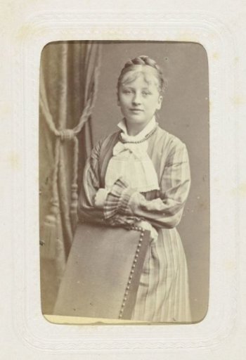 Studio portrait of a woman in a long dress behind a chair