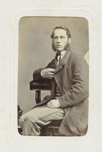 Studio portrait of a seated man with spectacles and sideburns