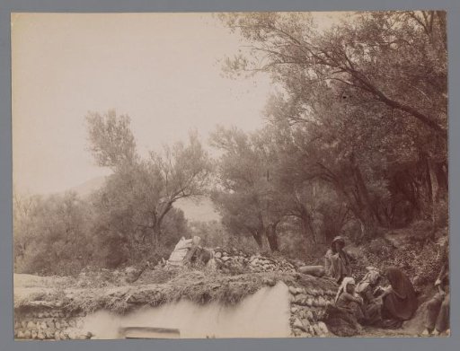 Group of men resting on the ground, along the roof edge of a white house, Iran