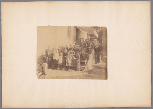 Photograph of a family on the steps in front of a house, location unknown.