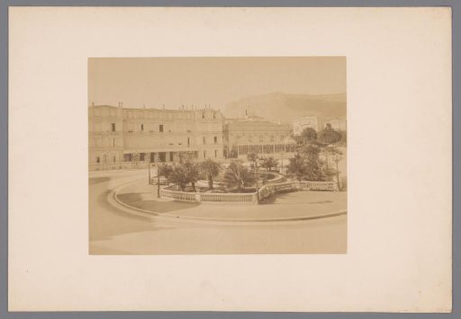 Square with a roundabout, palm trees, and a pond in the center, surrounded by houses