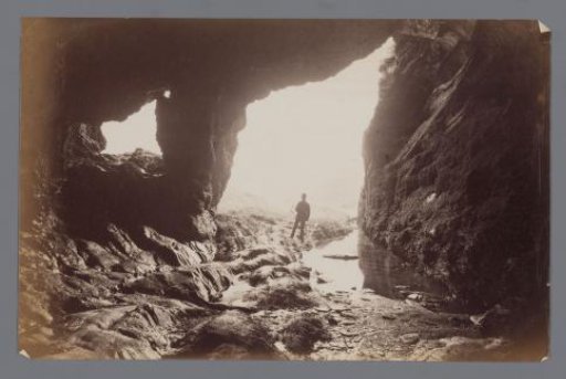 Man standing under a rock, next to water