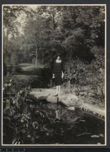 Portrait of G.A. Urtebise in a dark dress with a bowler hat standing by a pond