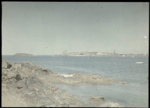 View of a river mouth, with rocks in the foreground and a city in the background