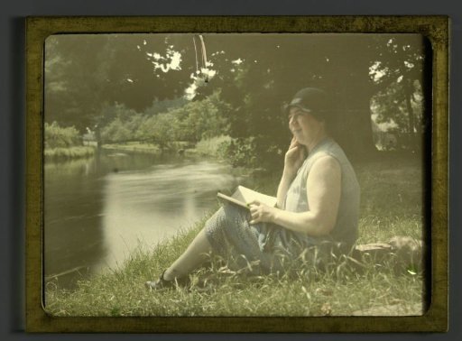 Portrait of Tine sitting on the bank of a river, looking up from a book