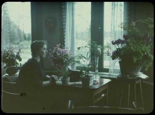 Portrait of Tine seated by a window, surrounded by flowers in vases, pots, and a basket