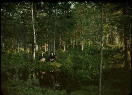 Fifi and Jan Olie seated on the shore of a lake in a forest