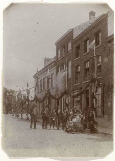 Decorated street for the inauguration or a visit of Queen Wilhelmina and Prince Hendrik, with men and children posing in the foreground