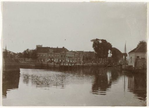 Houses along a quay, seen from the water, with a blunt church tower in the background, probably in the Netherlands