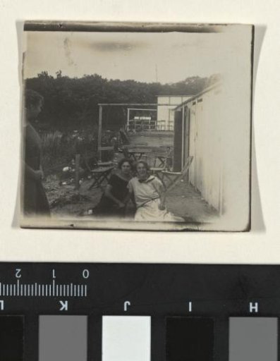 Two women sitting next to a row of changing rooms on the beach at Valkeveen