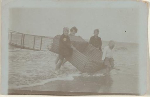 Koosje, Daan and Ben Ochse and another boy carrying a wicker beach chair out of the sea