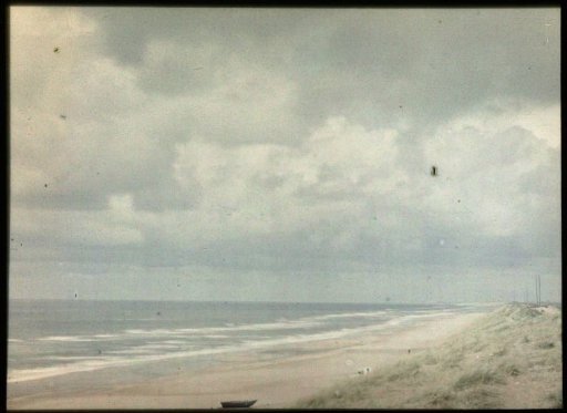 View (from a dune) over the North Sea beach, with beach grass in the lower right and a boat on the beach in the lower center