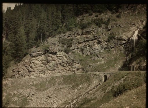 View of a mountainside, cut through by a road, with a chapel (?) on the right