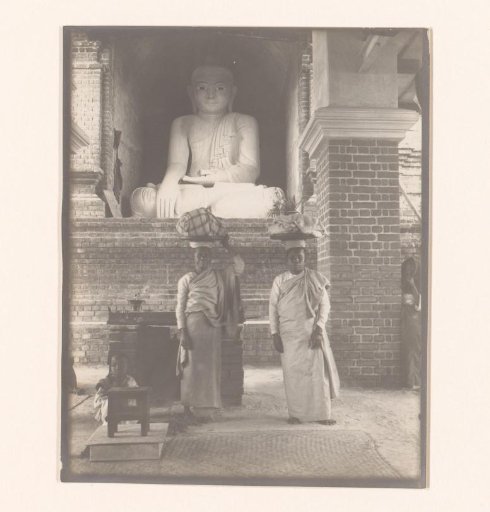 A man and a woman with items on their heads and a child in front of a statue of Buddha, Myanmar