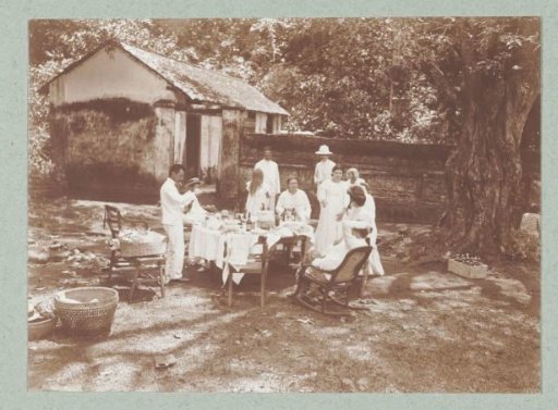 A set table in the tropics with people dressed in white seated at it.