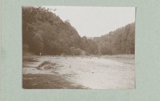 River flowing through the valley of a wooded mountain landscape with a footbridge over the river