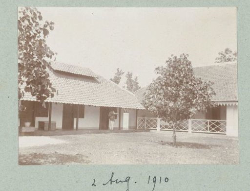 The inner courtyard of several houses with a staff member on the veranda holding a tray