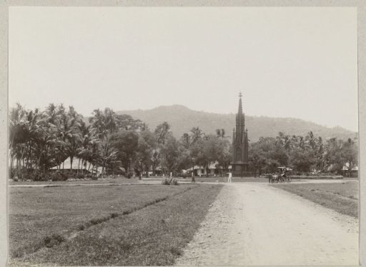 Monument on a square in the Dutch East Indies with a carriage and a velocipede in front of it