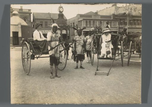 Two rickshaws and their bearers, with two women as passengers