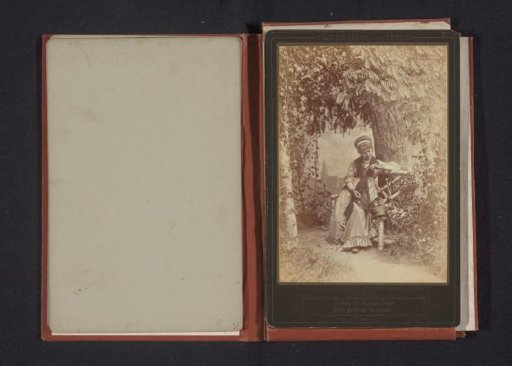 Portrait of an unknown woman seated on a bench before a tree, apparently looking at a ring on her finger