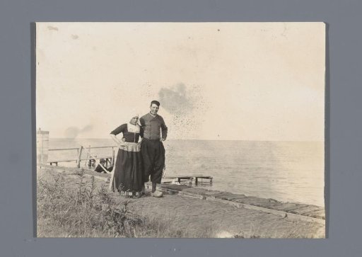 Two men in traditional dress (the left one in female attire) on a quay at Volendam, with the Zuiderzee in the background
