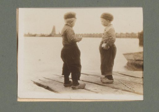 Two boys in traditional dress standing on a jetty by a lake