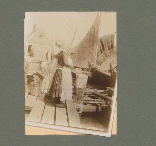 Two women in traditional dress standing on a scaffold between sailing boats