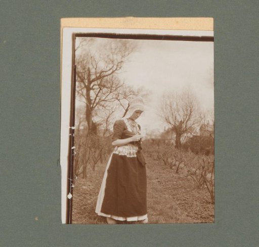 Woman in traditional dress with knitting, standing among bare trees