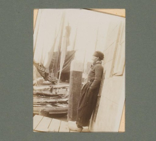 Man in traditional dress, standing on a pier between sailing boats