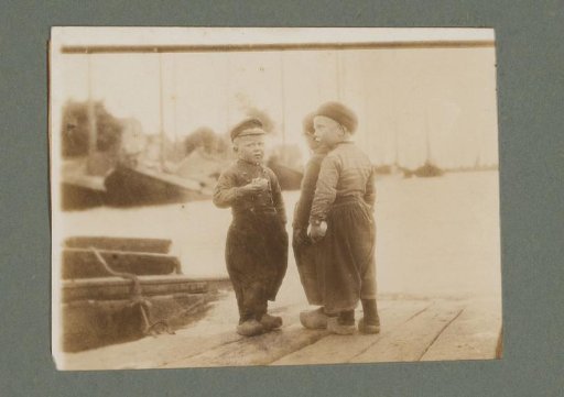 Three boys in traditional dress, standing on a pier