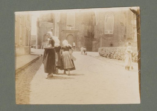 Three girls in costume seen from behind, the one at the back looking back