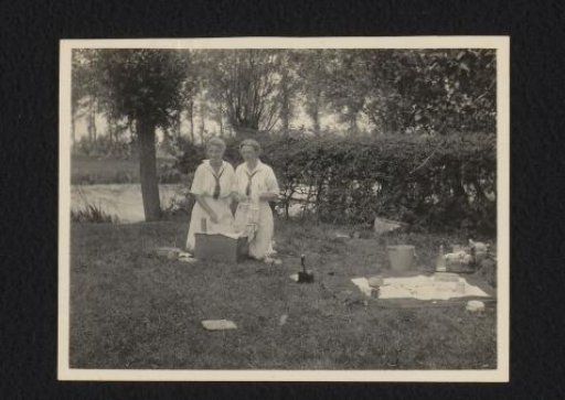 Two women washing dishes in the grass