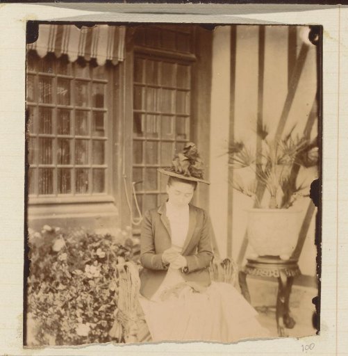 Portrait of a woman with a hat, seated in front of a house