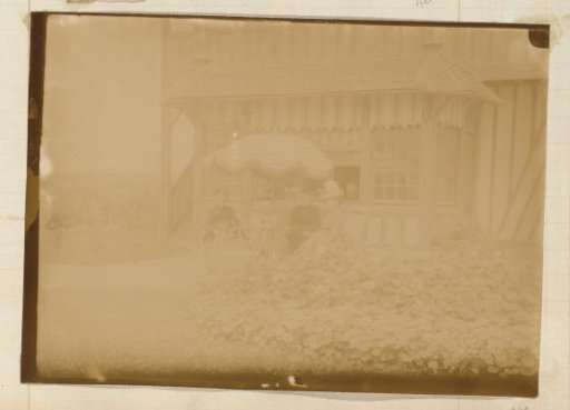 Three women seated at a table under a parasol in front of a half-timbered house