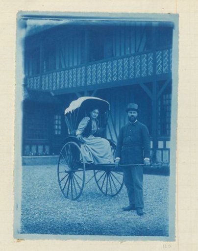 Portrait of a man and a woman, she seated in a carriage, he standing beside it holding the shaft