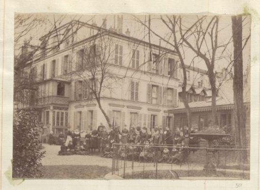 Group portrait of girls and teachers in front of a school with French inscription