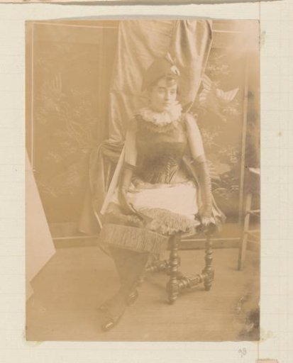 Portrait of a girl in a fringed dress, with fan, gloves and hat, seated before a room screen