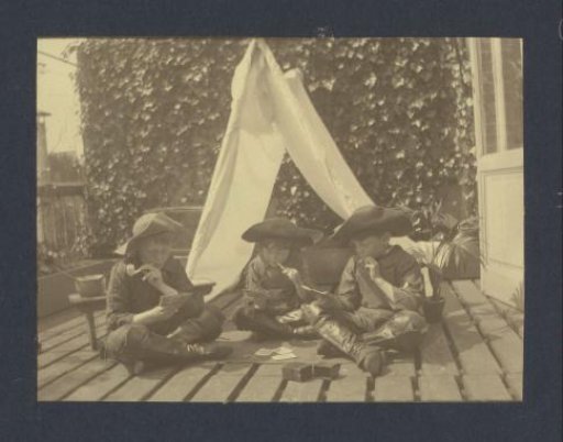 Three boys in costumes playing with playing cards in a homemade tent on the balcony