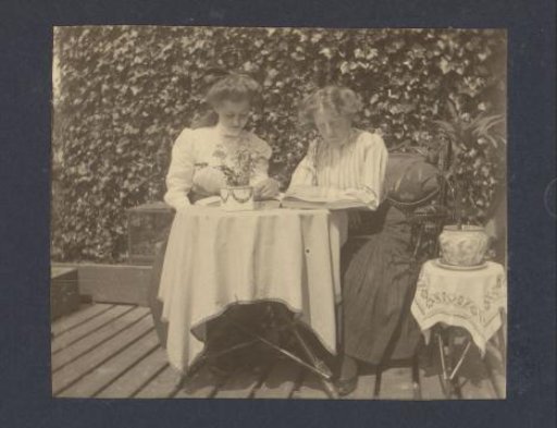 Two Young Women Reading at a Table on the Balcony