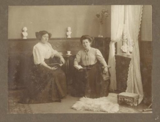 Two women seated in the corner of a room with a book in hand