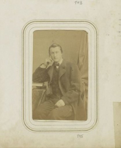 Portrait of a man in a long coat leaning on a pile of books
