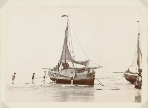 Boys with rolled-up trousers beside a beached fishing boat on the beach at Scheveningen