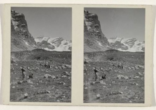Three walkers on a stony field with the snow-capped peaks of a mountain landscape in the background
