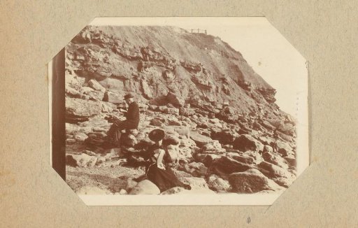 Reading man and woman with needlework among rocks on the coast