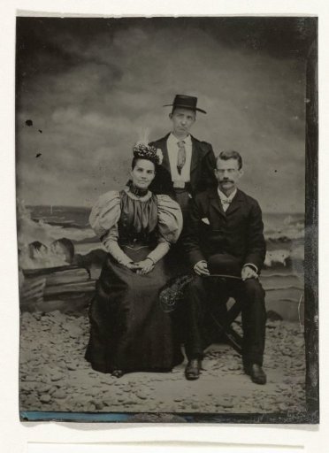 Portrait of two men and a woman before a painted backdrop depicting the sea