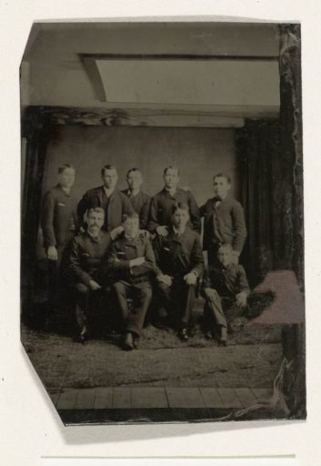 Group portrait of nine men in an atelier, with a white reflector screen in the ceiling