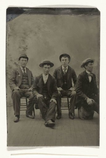 Portrait of four men with hats, seated in an atelier with a painted backdrop
