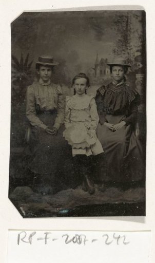 Portrait of two women and a girl, seated in a studio with a painted backdrop